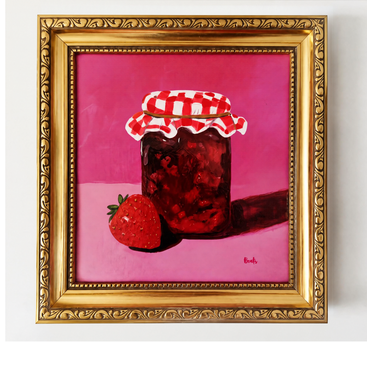 A framed painting of a glass jar of jam with a red-and-white checkered cloth lid and a strawberry on a pink background, enclosed in an ornate gold frame.